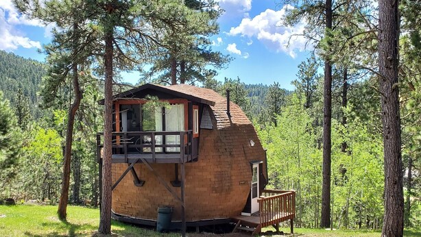 A wooden cabin with a balcony, surrounded by trees.