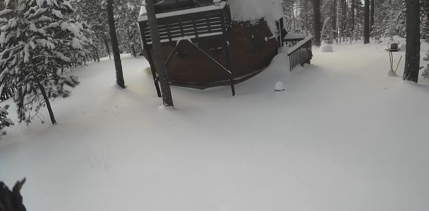 En snedækket træhytte med en terrasse og en lille veranda.