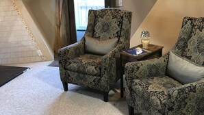 A cozy room with patterned armchairs, a small table with a lamp, and a view of the outdoors through a door.