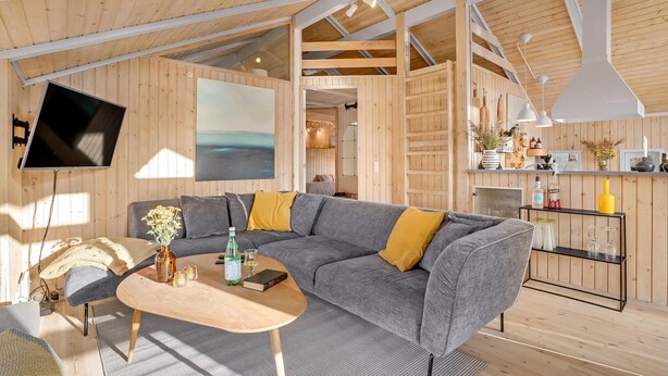 A modern, open-plan living space with a large gray sectional sofa, a wooden dining table, and a kitchen area with a white pendant light. - Awesome home in Juelsminde with WiFi (Juelsminde)