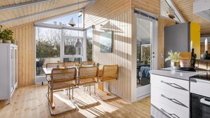 A modern kitchen with wooden cabinetry, a dining area with wicker chairs, and large windows offering views of the outdoors. - Awesome home in Juelsminde with WiFi (Juelsminde)