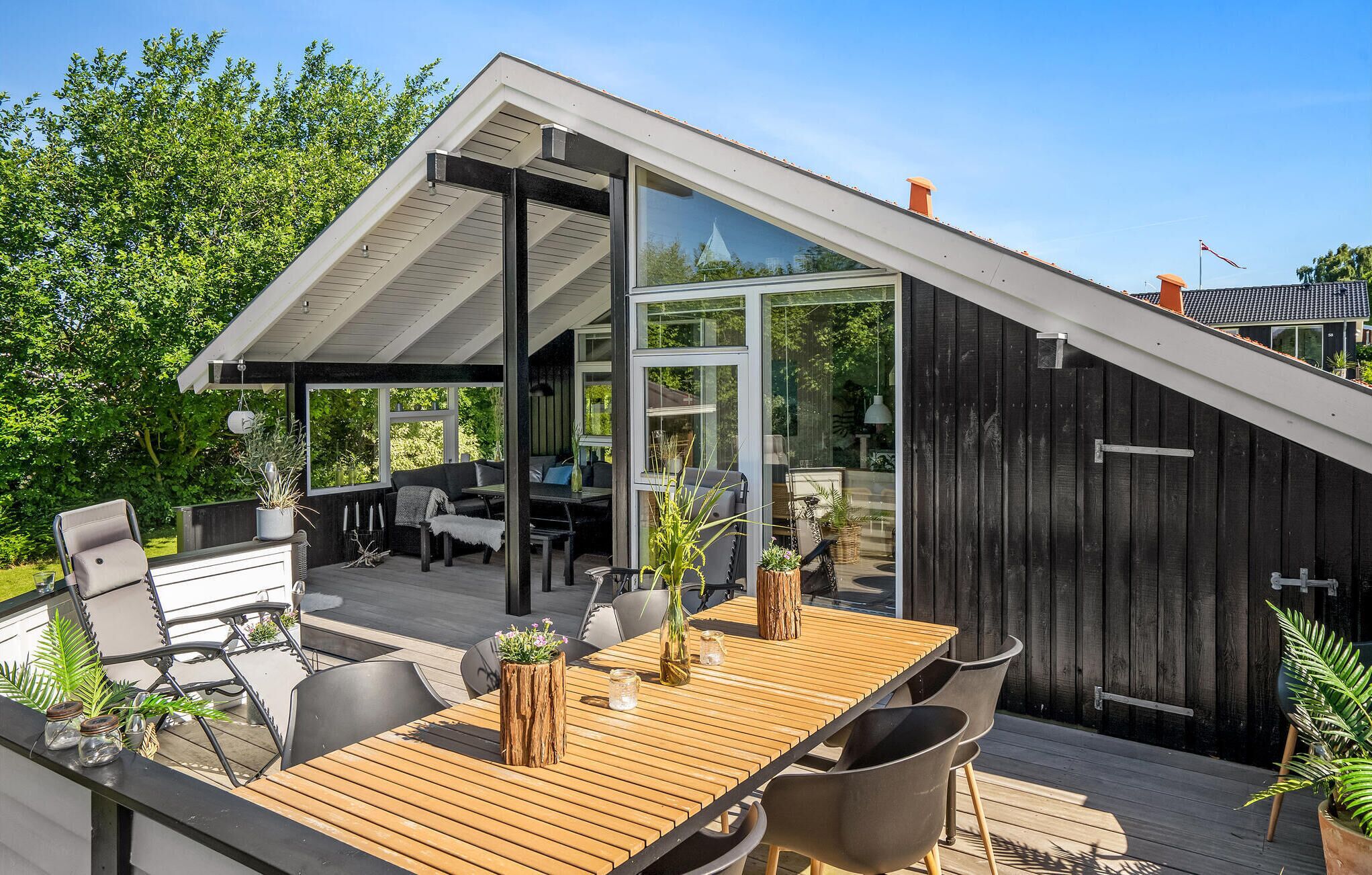 Una casa moderna con terraza de madera, comedor y zona de estar cubierta al aire libre.