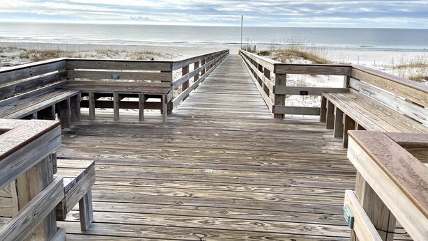 A wooden boardwalk leading to a beach with benches on either side.
