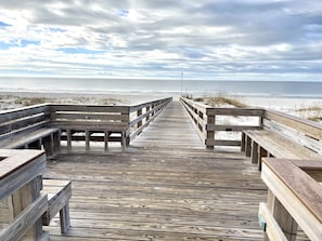 A wooden boardwalk leading to a beach with benches on either side.