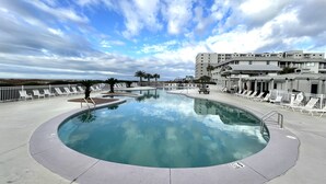 A large, circular swimming pool with lounge chairs and palm trees, surrounded by a white fence and buildings in the background.