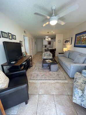 A living room with a TV, sofa, coffee table, and a ceiling fan.