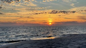 A sunset over a beach with a calm sea and a clear sky.