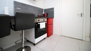 Una cocina compacta con un electrodoméstico negro y rojo, una puerta blanca y salpicadero de azulejos.