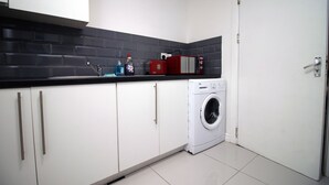 Una cocina compacta con armarios blancos, lavadora y un microondas rojo sobre la encimera.
