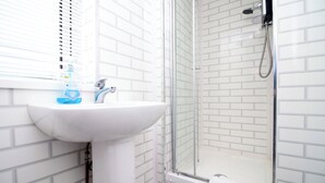 Un baño con lavamanos blanco, cabina de ducha de vidrio y una ventana con persianas.