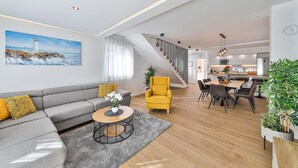 Una sala de estar moderna con un sofá, un sillón amarillo, una mesa de comedor y una escalera que lleva a la cocina.