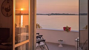 A balcony with a view of a sunset over a body of water, a clock, and some potted plants. - 1 bedroom beach front home in Siracusa (Siracusa)