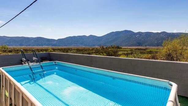 Una piscina rectangular con fondo de azulejos azules brillantes, rodeada por una plataforma de concreto, con montañas y vegetación escasa al fondo.