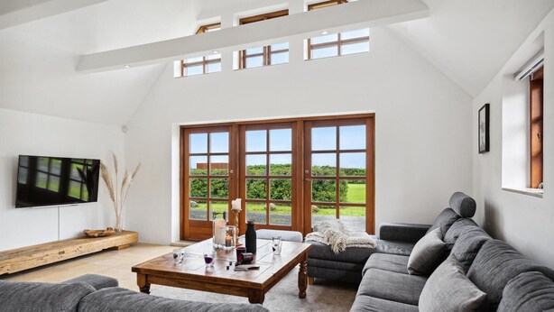 A spacious living room with a large wooden coffee table, grey sofas, and a television on the wall.