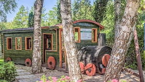 Una cabaña rústica de madera con puerta, ventanas y un letrero, rodeada de árboles y flores rosadas.