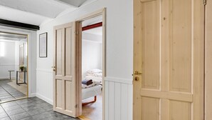 Ein Flur mit zwei Holztüren, davon eine geöffnet, die in ein Schlafzimmer mit Bett und Nachttisch führt.