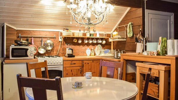 A cozy kitchen with wooden cabinets, a stove, a microwave, and a chandelier.