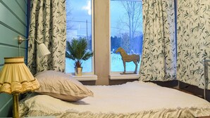 A bedroom with a bed, a lamp, a window with a view of trees and a horse statue, and a potted plant.