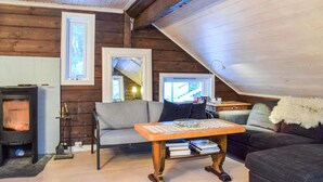 A cozy attic room with a wooden interior, a fireplace, a sofa, a table with books, and a television.