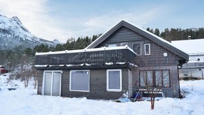 A two-story house with a sloped roof and large windows, surrounded by snow and mountains.