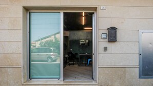 En bygningseingang med skydedør, et lille receptionsområde med bord og stole, og en fastmonteret postkasse.