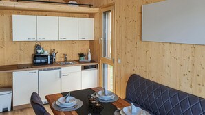 Una cucina compatta con pensili bianchi, un forno a microonde e un lavello. È presente un tavolo da pranzo apparecchiato con piatti e una panca imbottita nera.