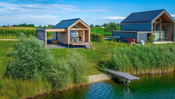 Due moderne cabine con facciata in legno, un'area salotto esterna coperta e un pontile che si estende in un lago tranquillo.