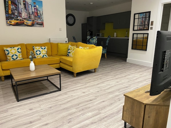Uma sala de estar moderna com um sofá amarelo, uma mesa de centro e uma televisão de tela plana.