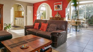 A living room with a brown leather sofa, a wooden coffee table, and a dining area with wicker chairs. - Amazing home in AGDE with WiFi (AGDE)