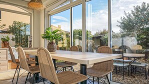 An outdoor dining area with wicker chairs and a table, large windows, and a view of the surrounding garden. - Amazing home in AGDE with WiFi (AGDE)