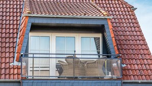 A residential building with a red-tiled roof, a balcony with wicker furniture, and a window with a white frame. - Gorgeous apartment in Friedrichskoog OT Frie (Friedrichskoog OT Frie)