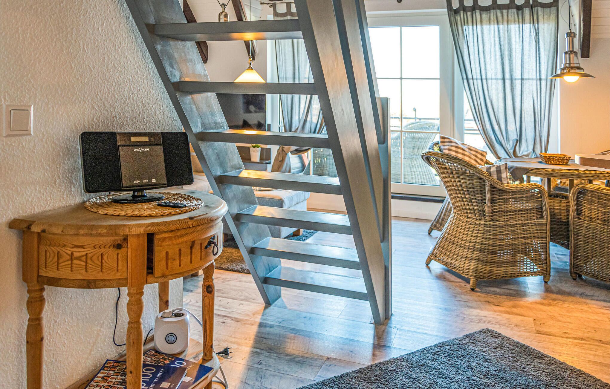 Um interior moderno com uma escrivaninha de madeira, um computador, uma escada, móveis de vime e vista pela janela.