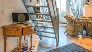 A modern interior with a wooden desk, a computer, a ladder, wicker furniture, and a view through a window. - Gorgeous apartment in Friedrichskoog OT Frie (Friedrichskoog OT Frie)
