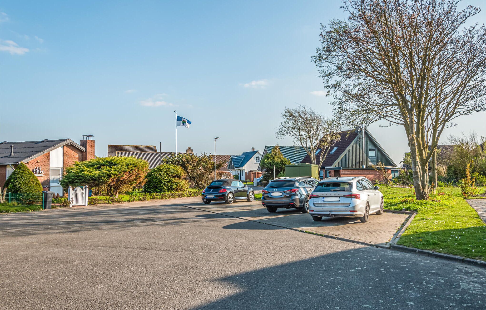 A residential street with houses, parked cars, and a flag on a flagpole.