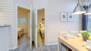 Ein moderner, offener Wohnbereich mit Holzvertäfelung, einem Essbereich mit Tisch und Stühlen sowie einem sichtbaren Schlafzimmer mit Bett und Fenster.