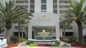 A hotel entrance with a fountain, palm trees, and a sign reading "The Pearl." - Beachfront with Beach Setup Included! (Navarre)