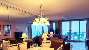 A spacious living area with a dining table, chairs, a sofa, and a balcony with a view. - Beachfront with Beach Setup Included! (Navarre)