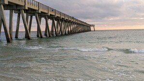 A pier extending into the water with a cloudy sky above. - Beachfront with Beach Setup Included! (Navarre)