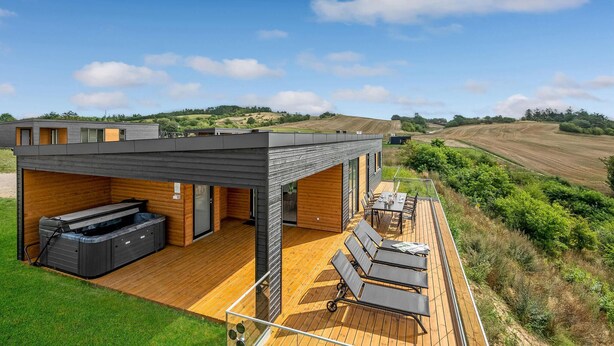 Una casa moderna con terraza, asientos exteriores y un jacuzzi.