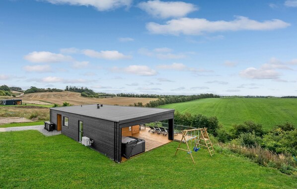 Una casa moderna con una amplia terraza, rodeada de campos verdes y un cielo despejado.