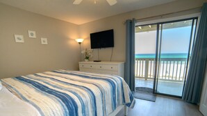 Una camera da letto con un letto, una cassettiera, una TV e un balcone vista spiaggia.