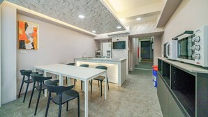 A modern kitchen with a white countertop, a microwave, and a sink. There is a dining area with a white table and black chairs. - Dingai Holiday Museum (Jiaoxi)