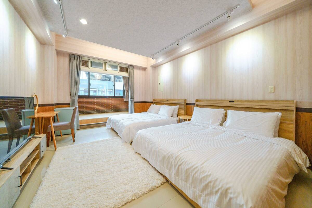 A hotel room with two beds, a desk, and a TV.