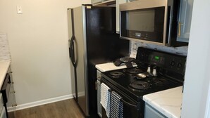 A kitchen with a black refrigerator, a microwave, a stove, and light blue cabinets. - Spacious Atl Gem near the Battery & Six Flags! (Mableton)