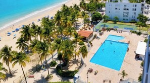 Un hotel frente al mar con piscina, palmeras y una cancha de baloncesto.
