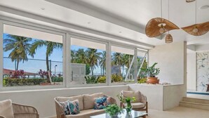 A modern living room with large windows, a sofa, a coffee table, and a hanging light fixture. - Beachfront  King Bed  Walk Everywhere (Carolina)