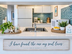 Una cucina con un frigorifero bianco, un lavello e un piano di lavoro con un cartello decorativo.