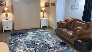 A living room with a large wardrobe, two bedside tables with lamps, a brown leather sofa, and a patterned rug. - Lovely Lovelock Landing (Lovelock)