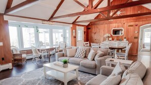 A spacious living room with a high ceiling, wooden beams, a sofa set, a dining area, and a kitchen visible through an open door. - Lake Winnipesaukee, Weirs Beach, Funspot, Gunstock (Laconia)