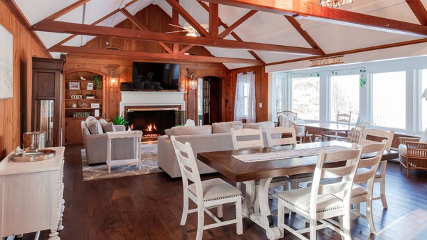 A spacious living room with a fireplace, wooden beams, and a large dining table with white chairs. - Lake Winnipesaukee, Weirs Beach, Funspot, Gunstock (Laconia)